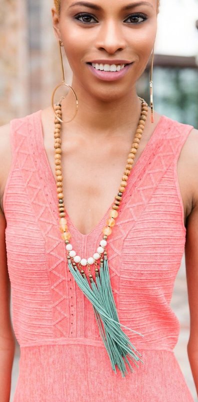 Long wooden-bead necklace with mint tassel worn over a coral knit dress
